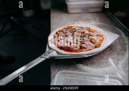 Préparation de pizzas traditionnelles italiennes. Le chef tient une longue pelle irob pour pizza, la pâte à pâte avec des pâtes et du fromage dans un four professionnel. Banque D'Images