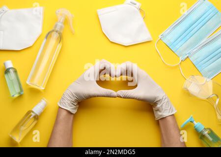Personne en gants montrant un geste cardiaque entouré d'articles médicaux sur fond jaune, vue du dessus Banque D'Images