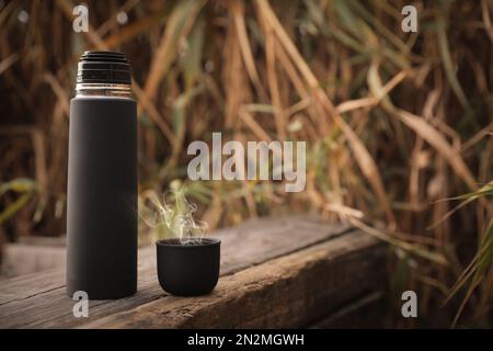 Thermos noirs et capuchon sur surface en bois à l'extérieur. Espace pour le texte Banque D'Images