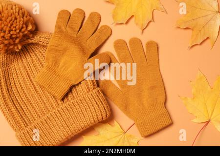 Élégants gants en laine, chapeau et feuilles sèches sur fond orange pâle, pose plate Banque D'Images