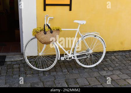 Vélo rétro près du mur jaune à l'extérieur avec fleurs dans le panier. Banque D'Images