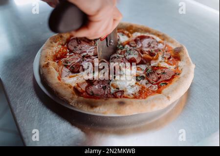 un homme coupe une pizza en morceaux. Gros plan main du boulanger de chef dans la pizza blanche uniforme de coupe à la cuisine Banque D'Images