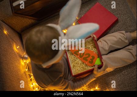 Un enfant sous le couvert d'un lapin tient une boîte rouge contenant une carotte avec les numéros du nouvel an 2023 Banque D'Images