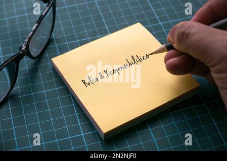 Une écriture manuelle rôles et responsabilités sur une note de papier de note jaune avec des lunettes sur un tapis de métier vert. Banque D'Images