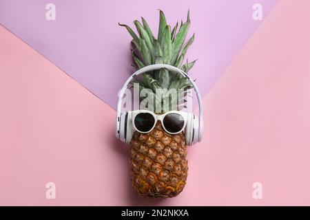 Ananas avec écouteurs et lunettes de soleil sur fond de couleur, vue du dessus. Concept créatif Banque D'Images