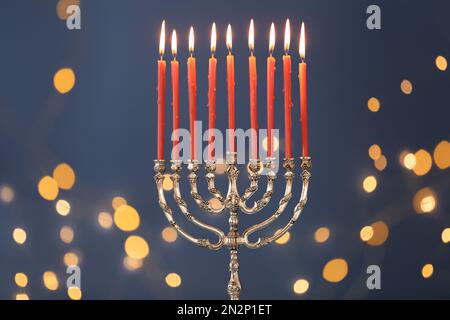 Menorah argentée avec bougies allumées sur fond bleu et lumières de fête floues. Célébration Hanukkah Banque D'Images