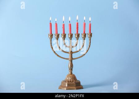 Menorah dorée avec bougies allumées sur fond bleu clair Banque D'Images