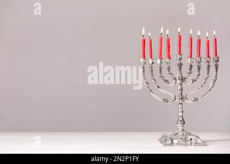 Menorah argentée avec bougies allumées sur la table sur fond gris clair. Célébration Hanukkah Banque D'Images