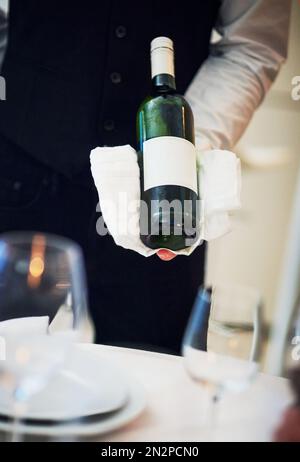 Garçon, table et serveur main avec vin et hospitalité tenant bouteille d'alcool. Barman, boissons et service d'un barman dans un restaurant gastronomique Banque D'Images