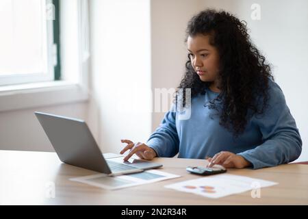 Femme hispanique concentrée travaillant à la maison, utilisant un ordinateur portable, espace de copie Banque D'Images