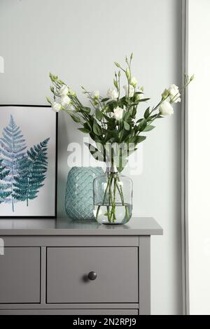 Composition avec des fleurs d'eustoma dans un vase en verre sur une armoire grise à l'intérieur Banque D'Images