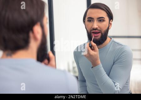 Beau jeune homme colorant ses lèvres à l'intérieur Banque D'Images
