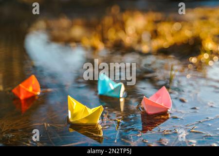 Bateaux en papier multicolores. Coloré rose jaune bleu orange navires dans la grande pouffle de neige de printemps sur la rue d'hiver. Temps chaud humide pluvieux, herbe ancienne. Bonjour Banque D'Images