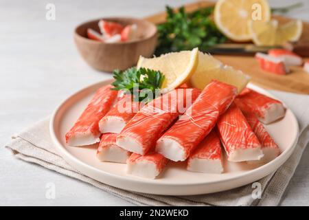 Assiette de bâtonnets de crabe frais avec citron sur table blanche, gros plan Banque D'Images