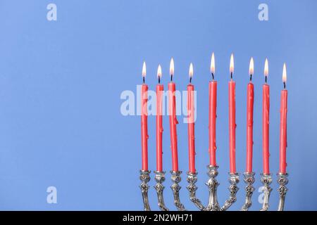 Menorah argentée avec bougies allumées sur fond bleu clair, espace pour le texte. Célébration Hanukkah Banque D'Images