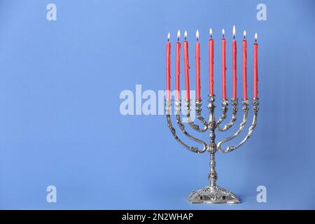 Menorah argentée avec bougies allumées sur fond bleu clair, espace pour le texte. Célébration Hanukkah Banque D'Images