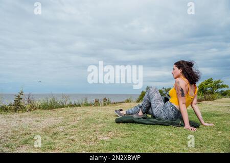 Jeune Latina Argentine, située sur l'herbe sur les rives du rio de la plata, sur le front de mer de Vicente Lopez à Buenos Aires, Argentine, Banque D'Images