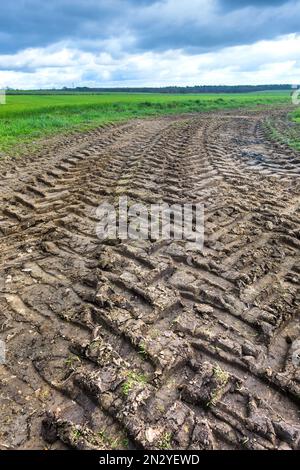 Chenilles de pneus de tracteur le long de la route de campagne boueuse - France. Banque D'Images