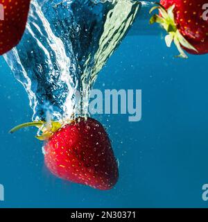les fraises mûres tombent dans l'eau soulevant des éclaboussures et des bulles d'air Banque D'Images
