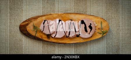 Tranches de Mortadella IGP de Bologne sur une planche à découper en bois rustique avec un glaçage au vinaigre balsamique de Modène Banque D'Images