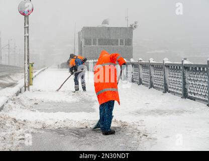 Services communautaires travailleurs dans le nettoyage uniforme passerelle de pont avec une pelle. Des ouvriers qui pelent de la neige au pont de Galata à Istanbul. Banque D'Images