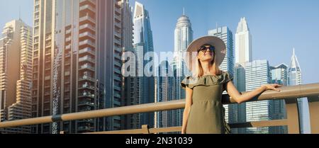 Femme de mode en robe verte et chapeau appréciant l'architecture de la ville de Dubaï. Les Émirats arabes Unis. bannière avec espace de copie Banque D'Images