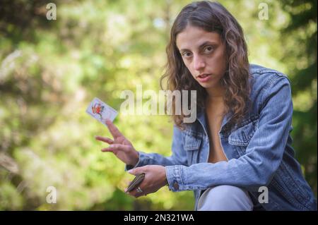 Jouer aux cartes dans le jardin de printemps. Une femme joue des cartes et tient un joker dans sa main. Banque D'Images