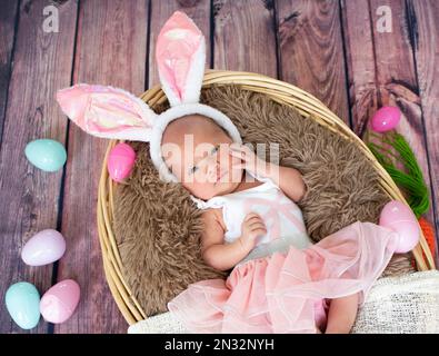 Bébé fille nouveau-né dans le panier de Pâques portant des oreilles de lapin. Banque D'Images