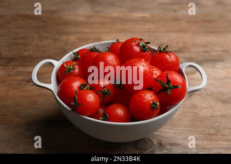 Tomates cerises fraîches mûres avec gouttes d'eau dans la passoire sur une table en bois Banque D'Images