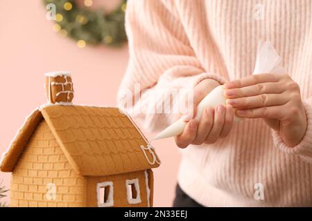 Femme décorant maison de pain d'épice avec glaçage sur fond rose, gros plan Banque D'Images