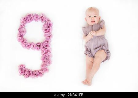 Petite fille de nouveau-né dans une barboteuse pourpre. bébé de 9 mois. Un jalon de neuf mois pour le bébé. Banque D'Images