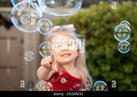 Petite fille jouant avec des bulles. Un enfant heureux qui éclate des bulles. Banque D'Images