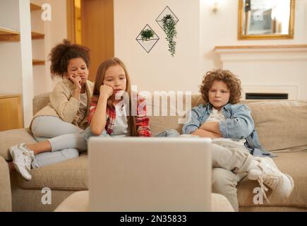 Trois enfants regardent quelque chose sur un ordinateur portable Banque D'Images
