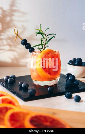 un cocktail de glace, de bleuets, d'une tranche d'orange fraîche, d'un verre arrondi, de romarin et de fruits frais. Banque D'Images