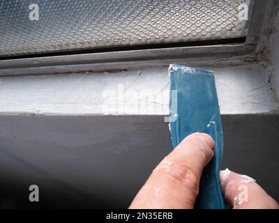 Hand's Man applique de la putty sur un mur blanc pour combler les fissures Banque D'Images