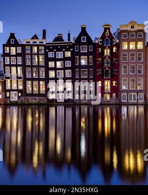 Amsterdam, pays-Bas - 18 janvier 2023 : paysage urbain de maisons traditionnelles hollandaises pendant l'heure bleue au canal de Damrak à Amsterdam avec réflexion Banque D'Images