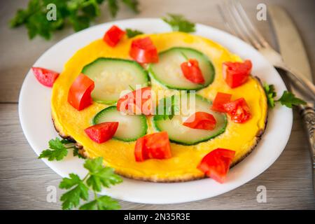 Omelette frite avec courgettes, tomates, herbes dans une assiette sur une table en bois. Banque D'Images