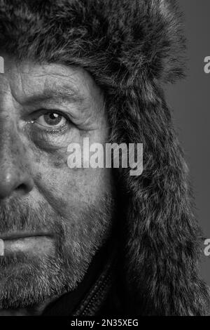 Gros plan demi-visage portrait noir et blanc d'un homme d'extérieur robuste et expérimenté, avec une barbe portant un aviateur de fourrure ou un chapeau de style trappeur Banque D'Images