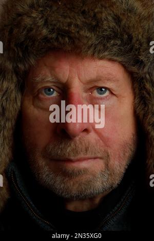 Portrait en gros plan d'un homme aventureux d'extérieur robuste et mature avec des yeux bleus et une barbe portant un aviateur de fourrure ou un chapeau de style trappeur Banque D'Images