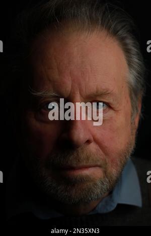 Dark moody Low Key gros plan tête portrait d'un homme mature et attrayant de 70 ans et plus avec barbe et yeux bleus Banque D'Images