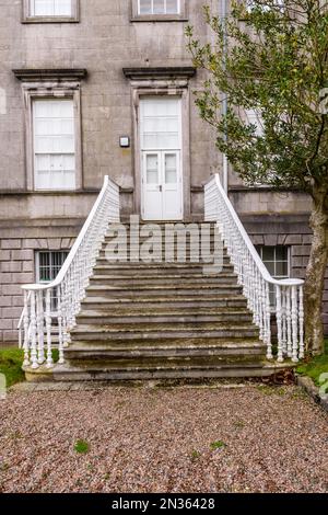 Des marches avec rambardes en fonte mènent à une porte blanche sur un vieux bâtiment. Banque D'Images