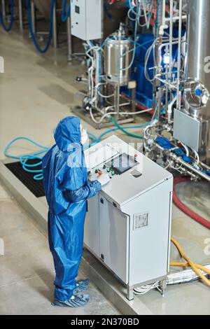 Portrait vertical de l'employé dans l'équipement de commande d'équipement de protection en usine, debout près du panneau de commande Banque D'Images