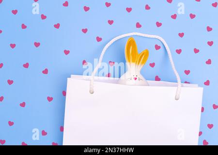 Shopping pour Pâques. Sac à provisions en papier blanc avec lapin blanc sur fond bleu et coeurs rouges. Concept cadeaux de Pâques, préparation, surprise de vacances Banque D'Images