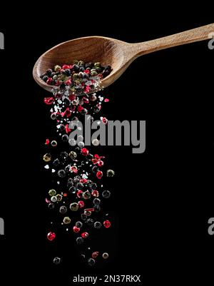 Mélange de différents grains de poivre et sel tombant de la cuillère en bois sur fond noir. Banque D'Images