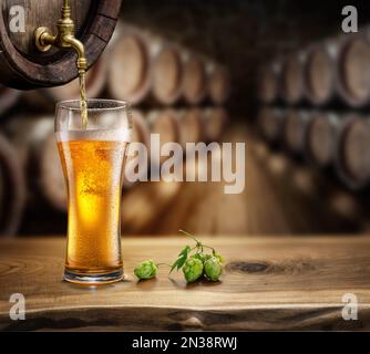 Verser de la bière dans un verre à partir d'un fût en bois. Cave de brasserie floue en arrière-plan. Banque D'Images