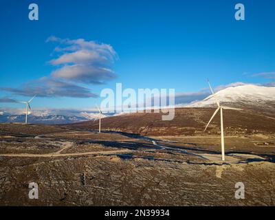 Moulins à vent sur les collines pendant le coucher du soleil. Énergies renouvelables, énergies vertes. Montagnes en arrière-plan avec de la neige. Énergie éolienne et écologique. Banque D'Images