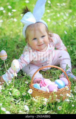 Enfant à la recherche d'œufs dans le jardin. Petite fille s'amusant sur la chasse aux œufs de Pâques. Enfant dans les oreilles de lapin et costume de lapin. Enfant en plein air. CELE Banque D'Images