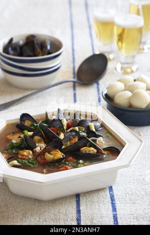 Bol de service de soupe de moules avec petits pains et bière sur une nappe en lin à rayures bleues Banque D'Images