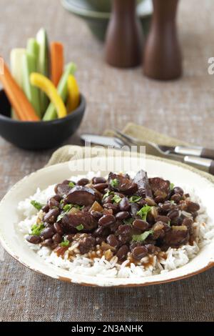 Haricots noirs avec saucisse sur le riz servis avec des bâtonnets de légumes crus Banque D'Images