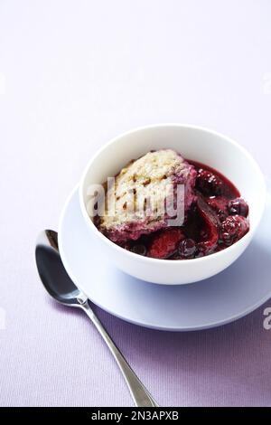 Bol de cobbler aux fruits rouges avec une garniture de biscuit et une cuillère sur fond violet Banque D'Images